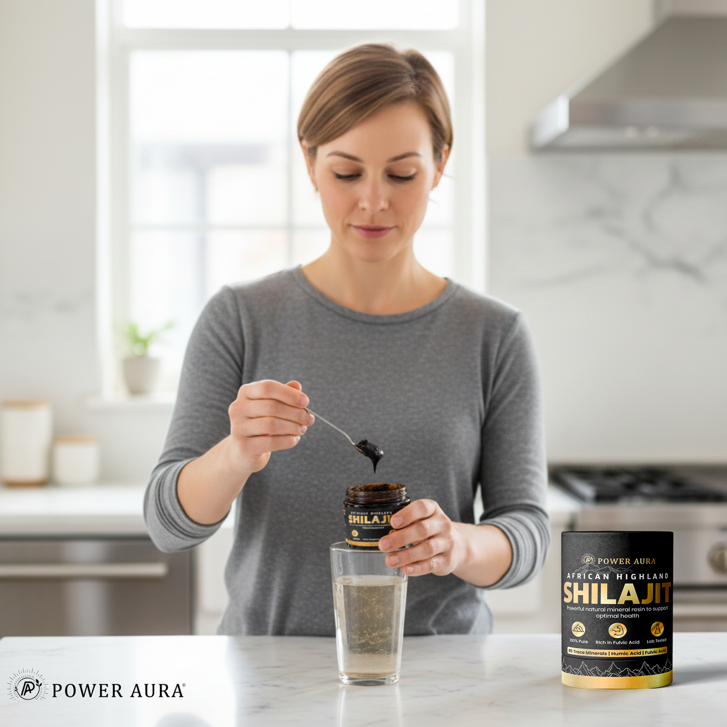 Woman in a kitchen pouring Shilajit into a glass with Power Aura branding.