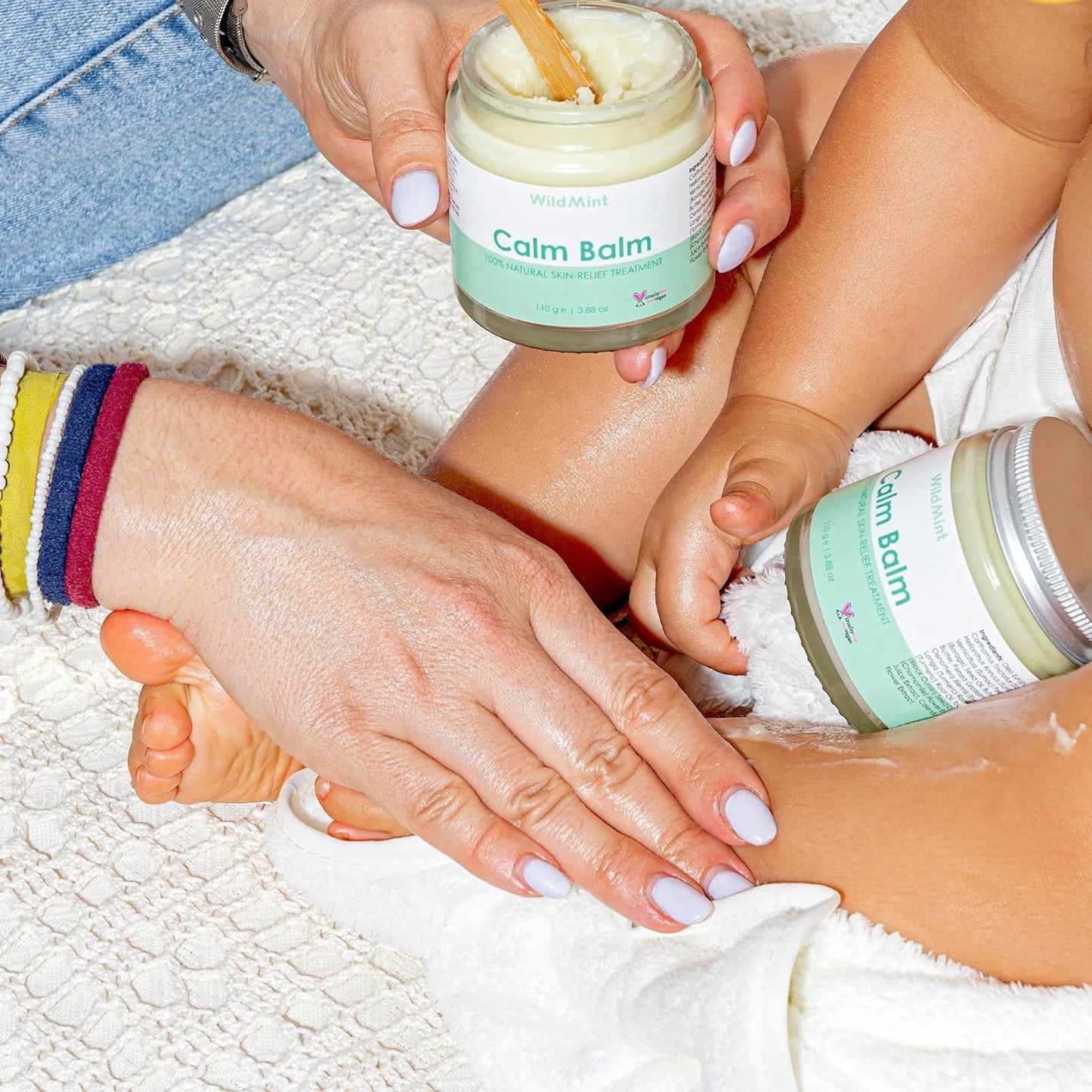 Person applying Calm Balm to a child's foot with another jar of the balm nearby.
