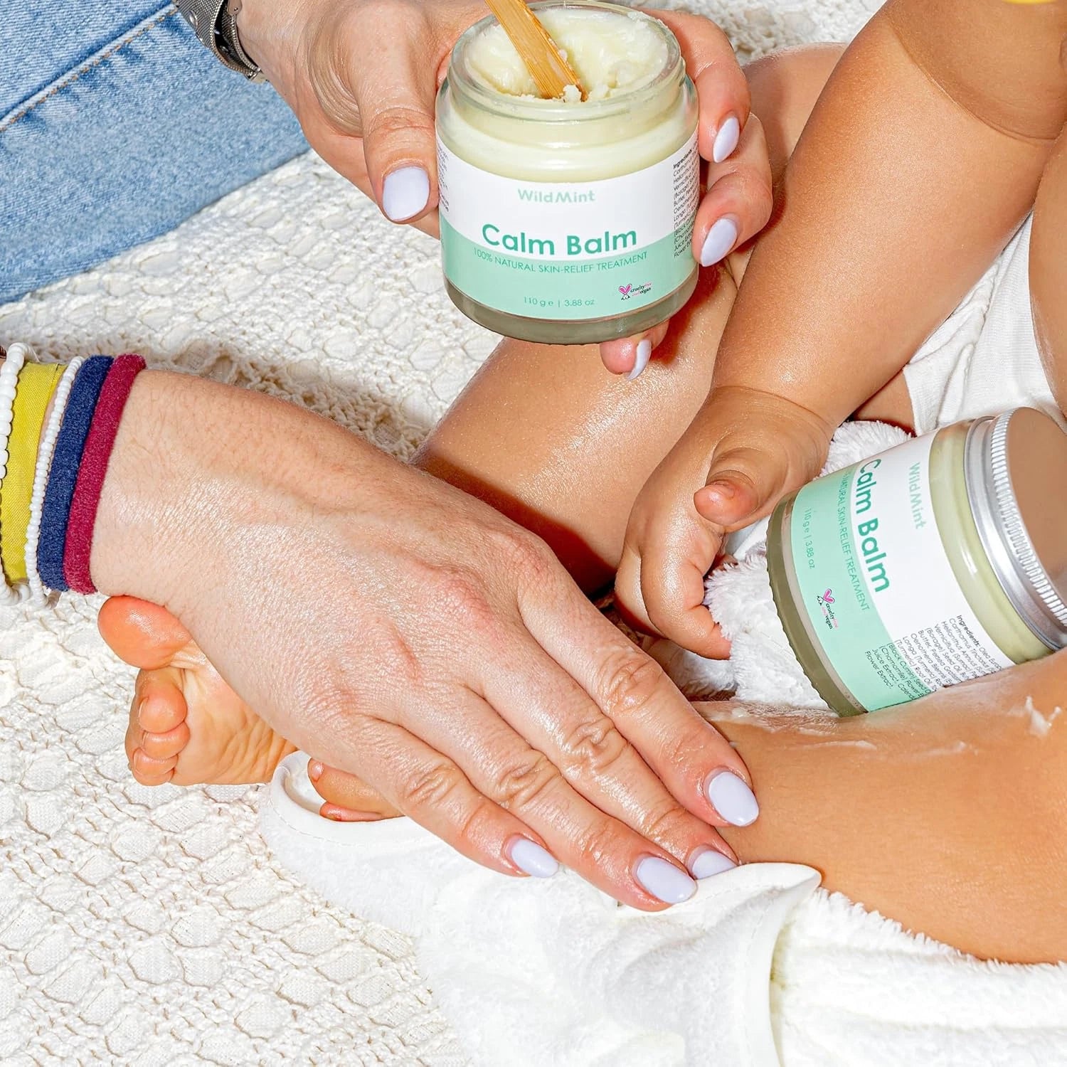 Person applying Calm Balm to a child's foot with another jar of the balm nearby.